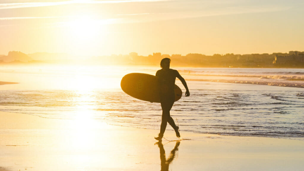 Mit Board am Strand laufender Surfer: Typischer Sport im Sommer