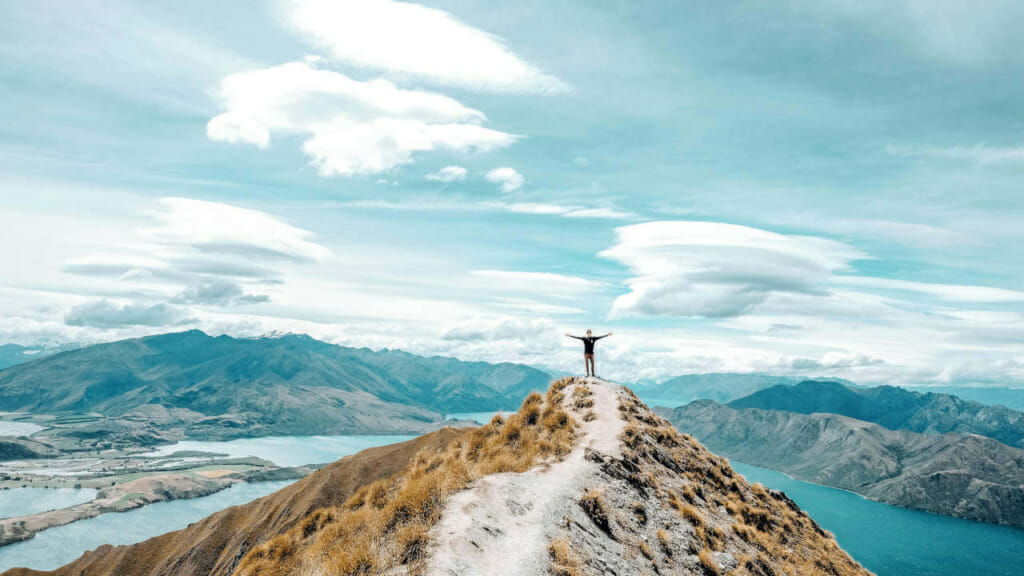 Person auf einem Berggipfel, die motiviert die Arme nach oben reißt