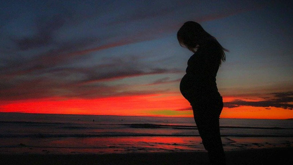 Schwangere Frau am Meer während des Sonnenuntergangs